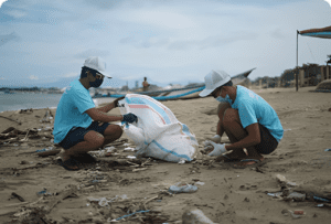Two people picking up litter on sand