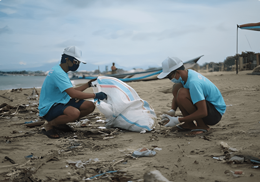 Two people picking up litter on sand